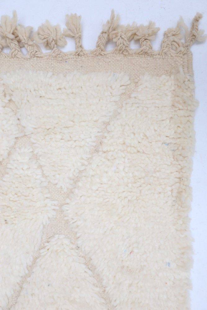 Tapis en texture douce de couleur crème avec un motif géométrique en relief et des franges décoratives.