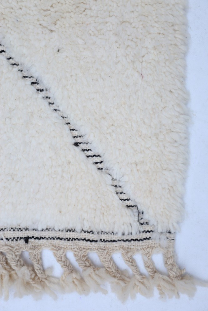 Tapis berbère en laine, crème avec des motifs géométriques noirs et des franges, ajoutant une touche chaleureuse et moderne.