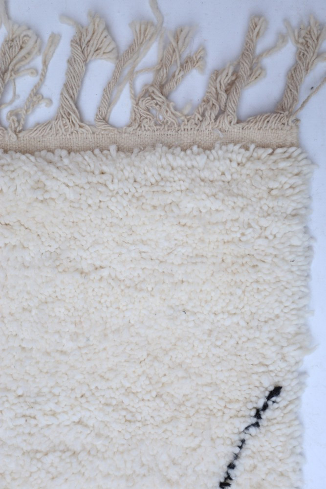 Tapis en laine beige aux motifs minimalistes et franges, créant une ambiance chaleureuse et moderne.