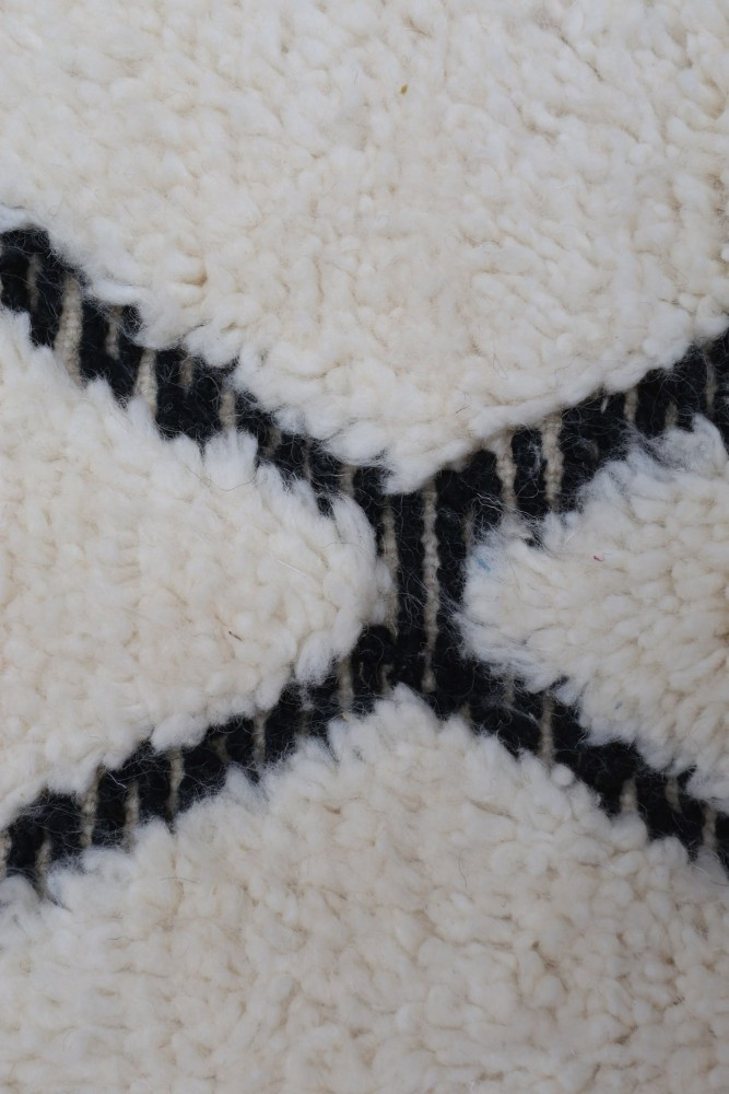 Tapis berbère blanc avec motifs géométriques noirs, ajoutant une touche de modernité et de chaleur à votre intérieur.