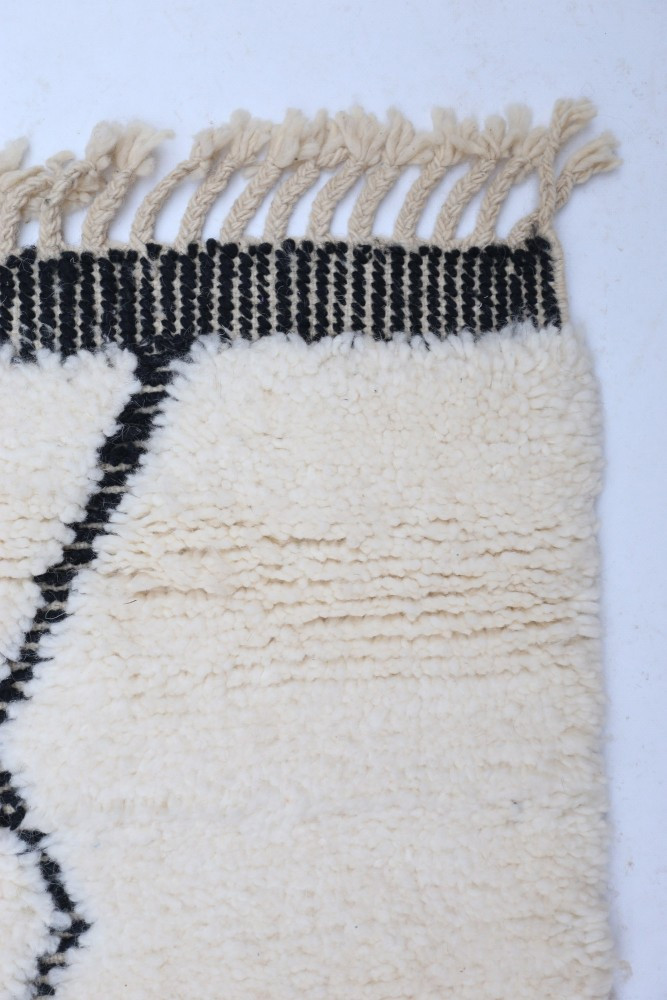 Tapis berbère blanc avec motifs géométriques noirs et franges, ajoutant une touche moderne et chaleureuse à votre intérieur.