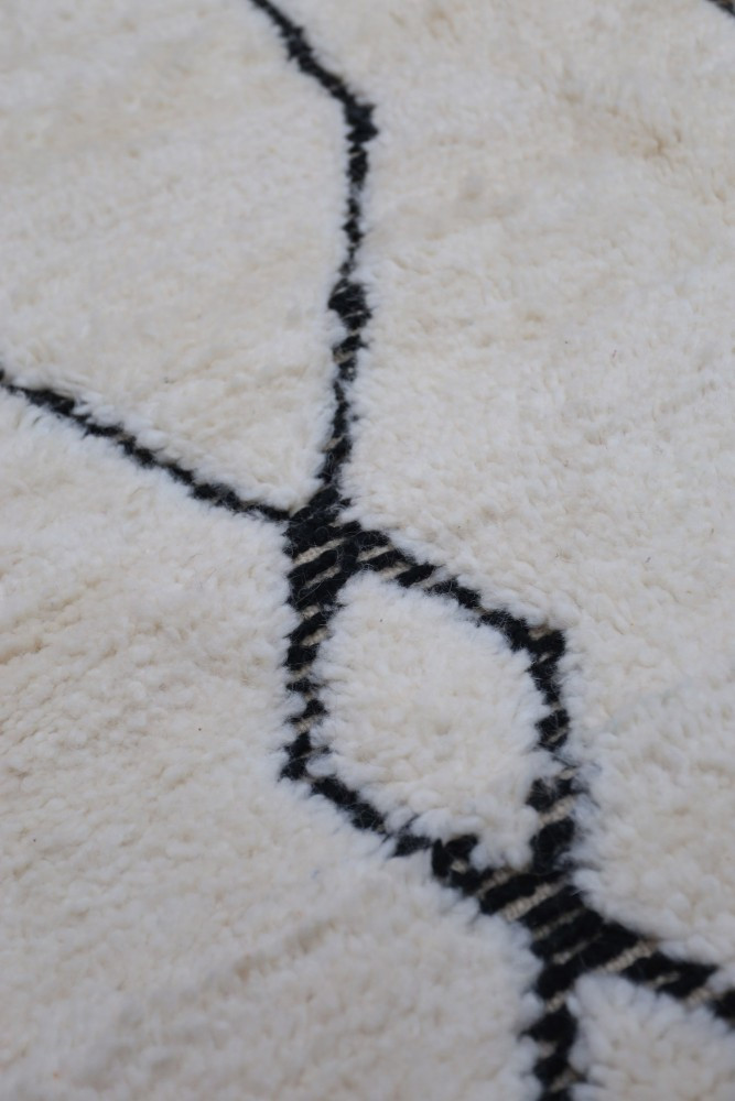 Tapis berbère en laine avec motifs géométriques noirs sur fond beige, ajoutant une touche moderne et élégante à votre intérieur.