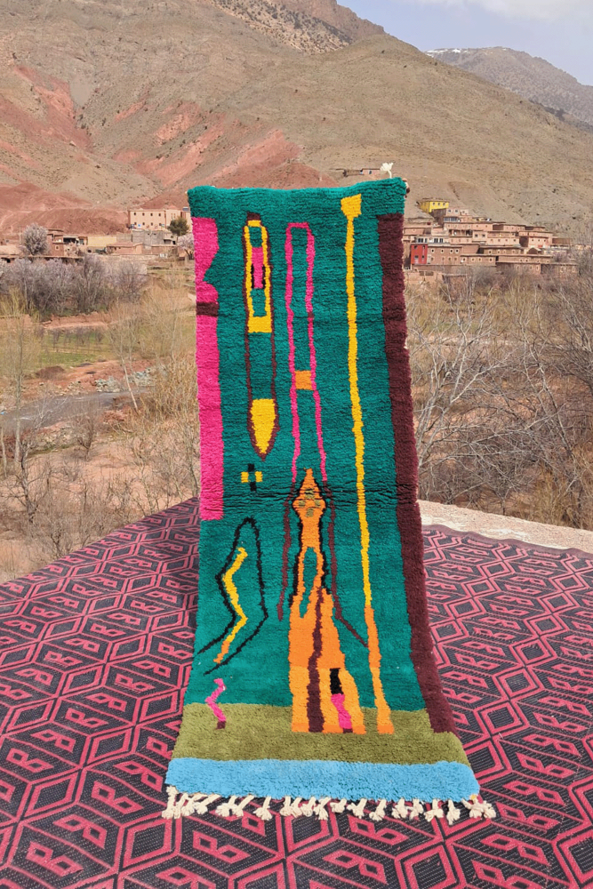 Tapis berbère coloré aux motifs géométriques, dominé par le vert, le rose et des touches de jaune.