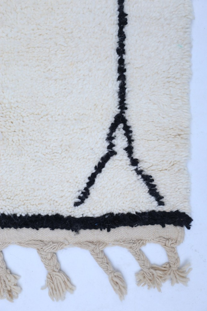 Tapis berbère doux en laine crémeuse avec des motifs noirs géométriques et des franges élégantes.