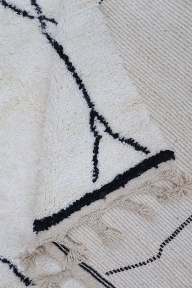 Tapis au style moderne avec des motifs géométriques noirs sur fond crème et des franges délicates.
