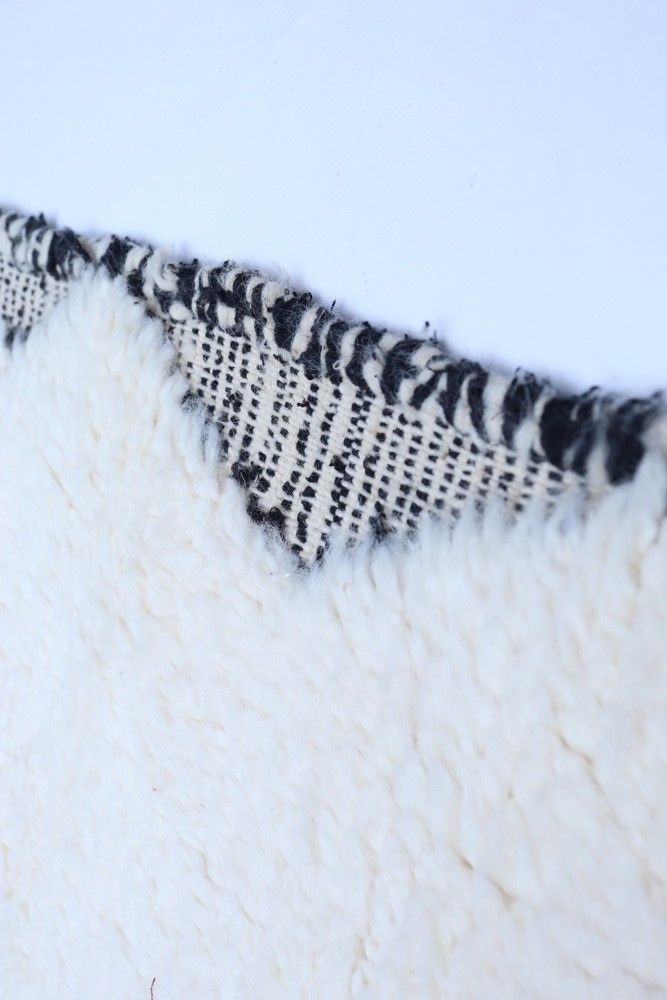 Tapis en faux poil blanc avec bord noir et motifs géométriques pour un style moderne et cosy.