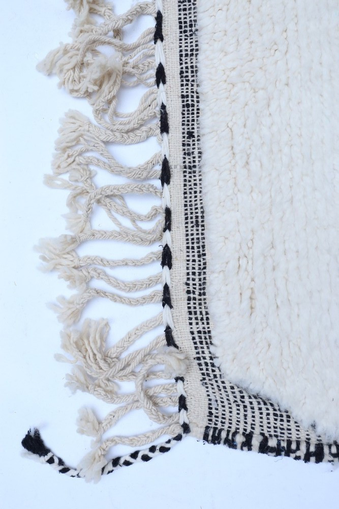 Tapis au design bohème, couleur crème avec des motifs géométriques noirs et des franges décoratives.