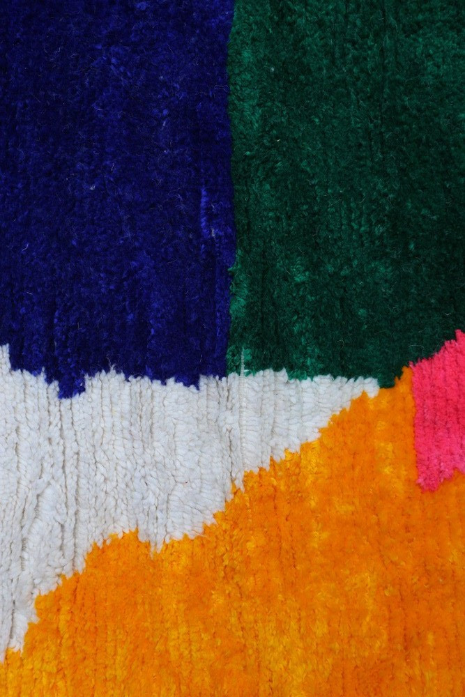 Tapis berbère coloré avec des motifs géométriques en vert, violet, rose, orange et blanc, ajoutant une touche moderne à la décor