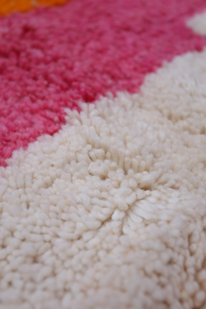 Tapis berbère coloré avec des motifs géométriques, dominé par des teintes blanches, roses et oranges.