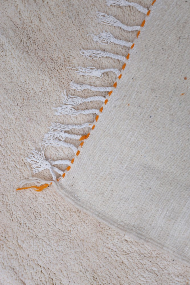 Tapis berbère au design minimaliste, couleurs beige et orange, avec des franges élégantes et un tissage artisanal.