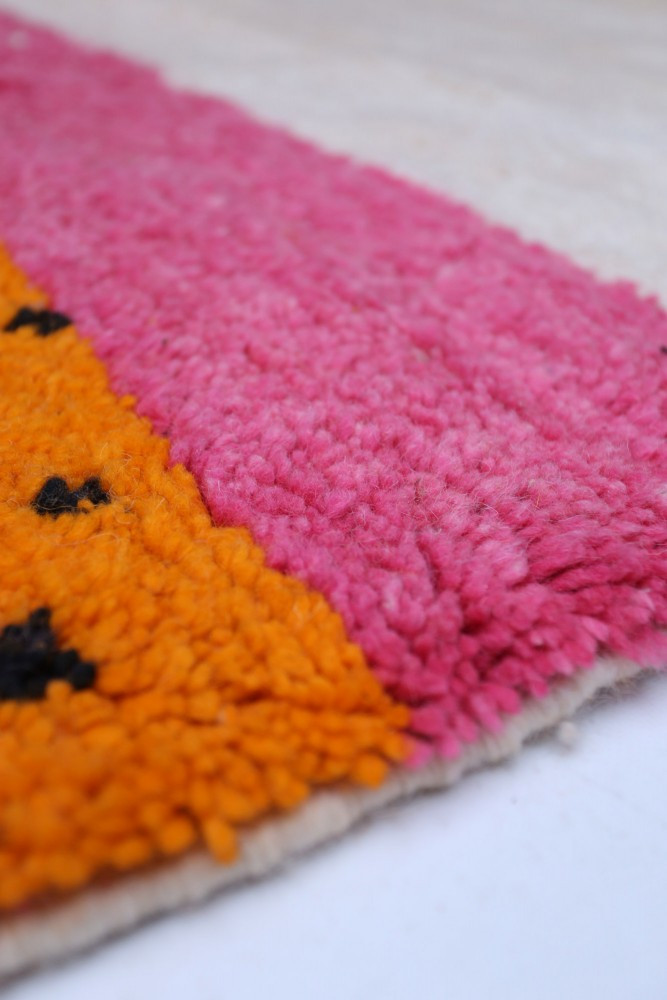 Tapis berbère coloré avec des motifs géométriques en rose, orange et noir sur fond crème.