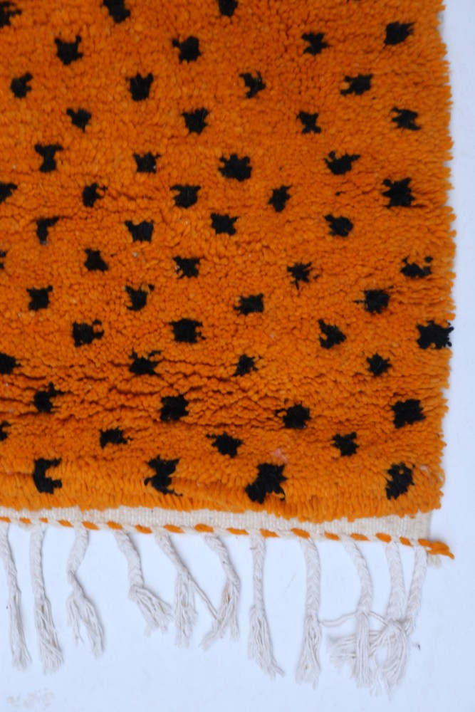 Tapis berbère en orange vif avec motifs noirs en points, offrant un style contemporain et chaleureux.