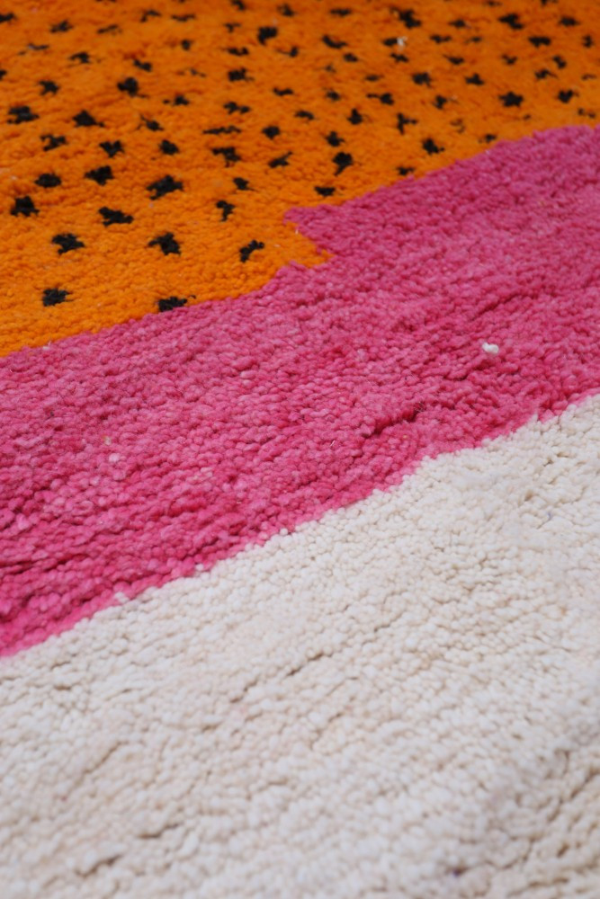 Tapis berbère moderne avec des motifs géométriques en orange, rose et crème, apportant une touche colorée et chaleureuse.