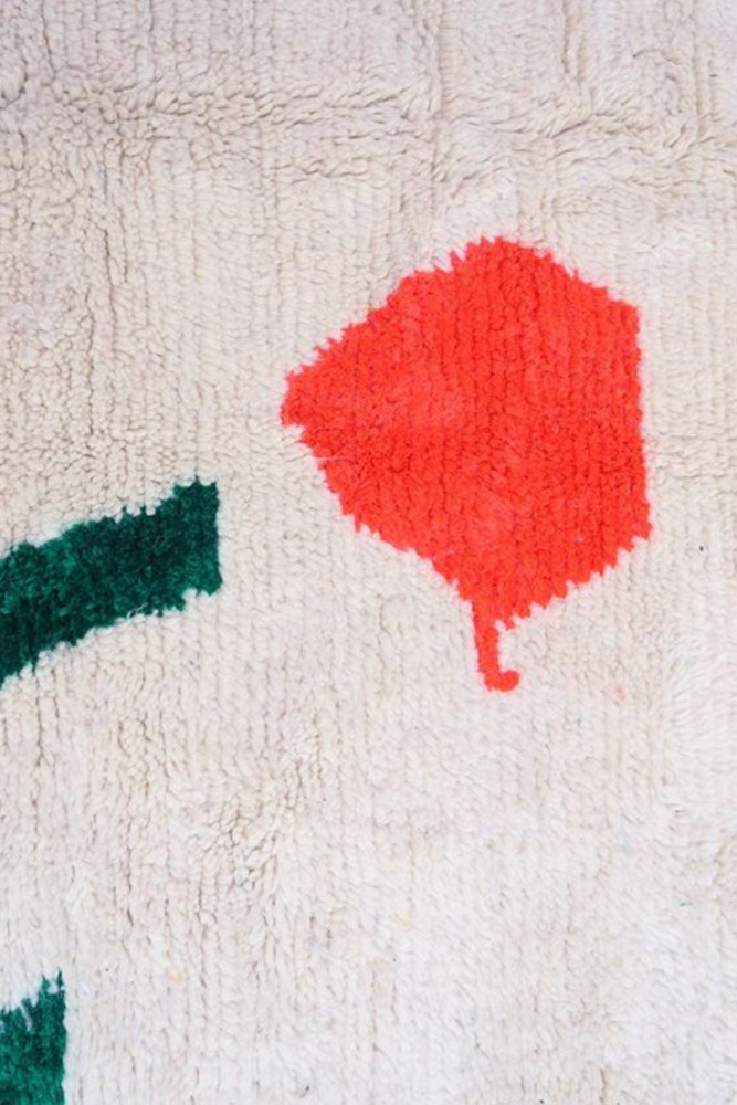 Tapis berbère aux motifs abstraits avec des couleurs vives comme le rouge et le vert sur fond crème.