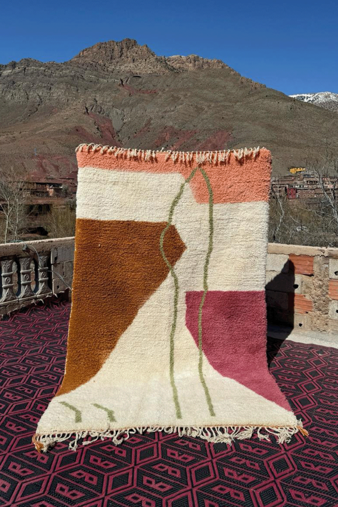Tapis berbère aux couleurs pastel, motifs géométriques avec des teintes rose, orange, et beige.