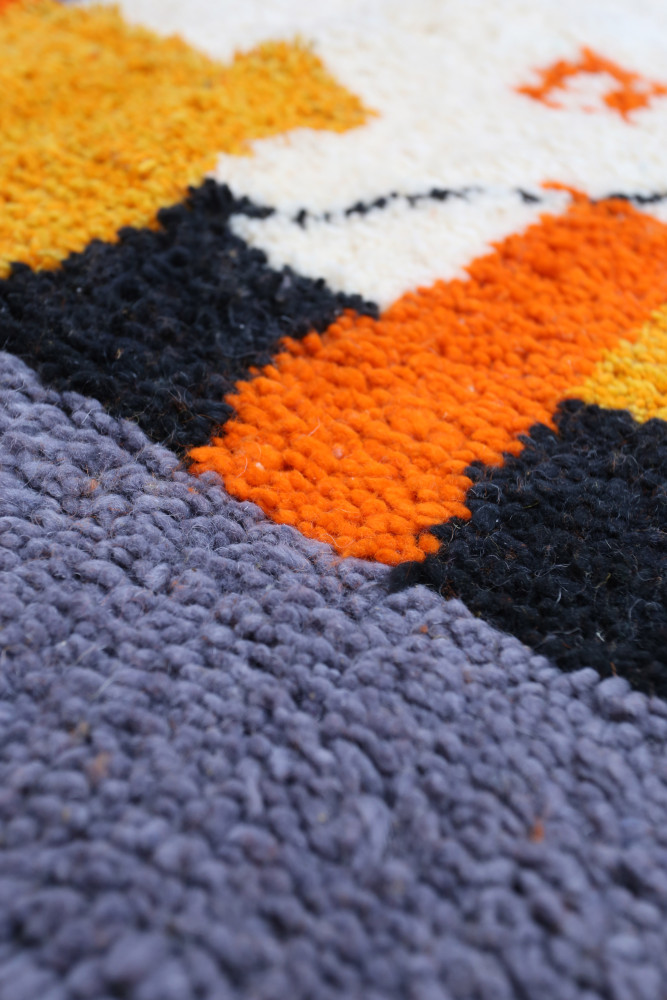 Tapis berbère à motifs géométriques avec des couleurs vives comme l\'orange, le noir et le violet.