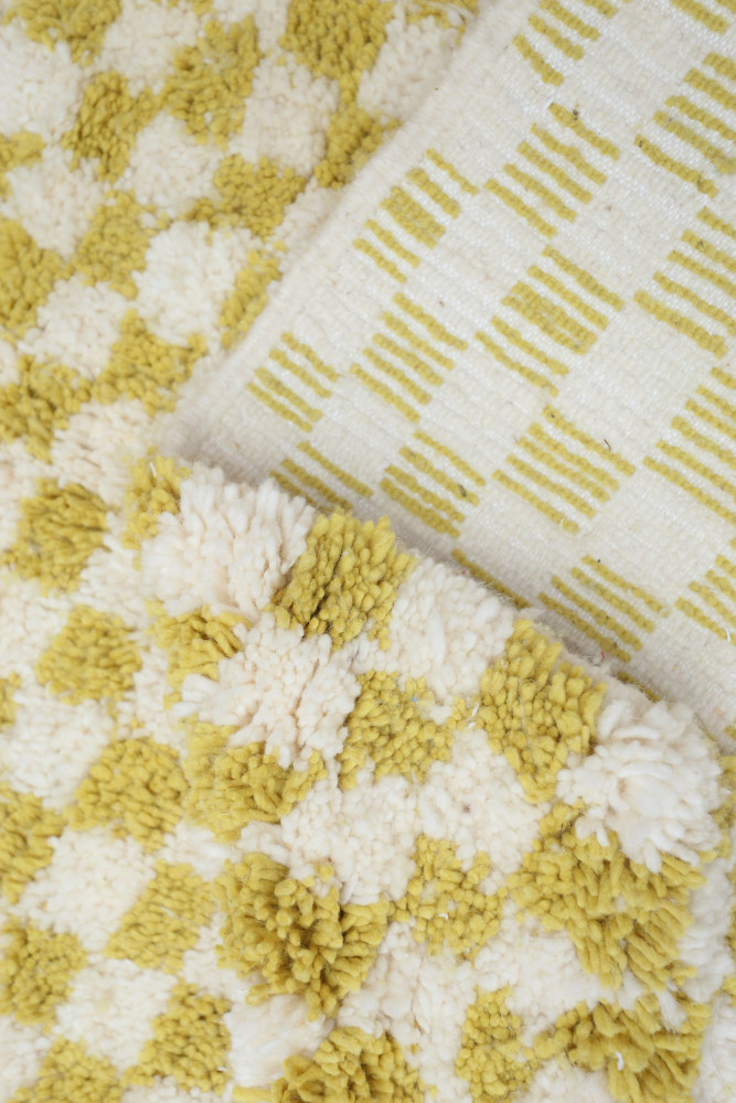Tapis berbère en laine avec motifs géométriques en jaune et blanc, offrant une texture douce et chaleureuse.