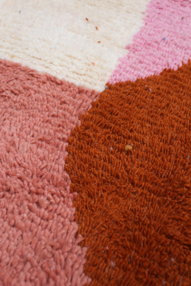 Tapis berbère à motifs géométriques dans des teintes de rose, crème et brun orangé, offrant une texture douce et chaleureuse.