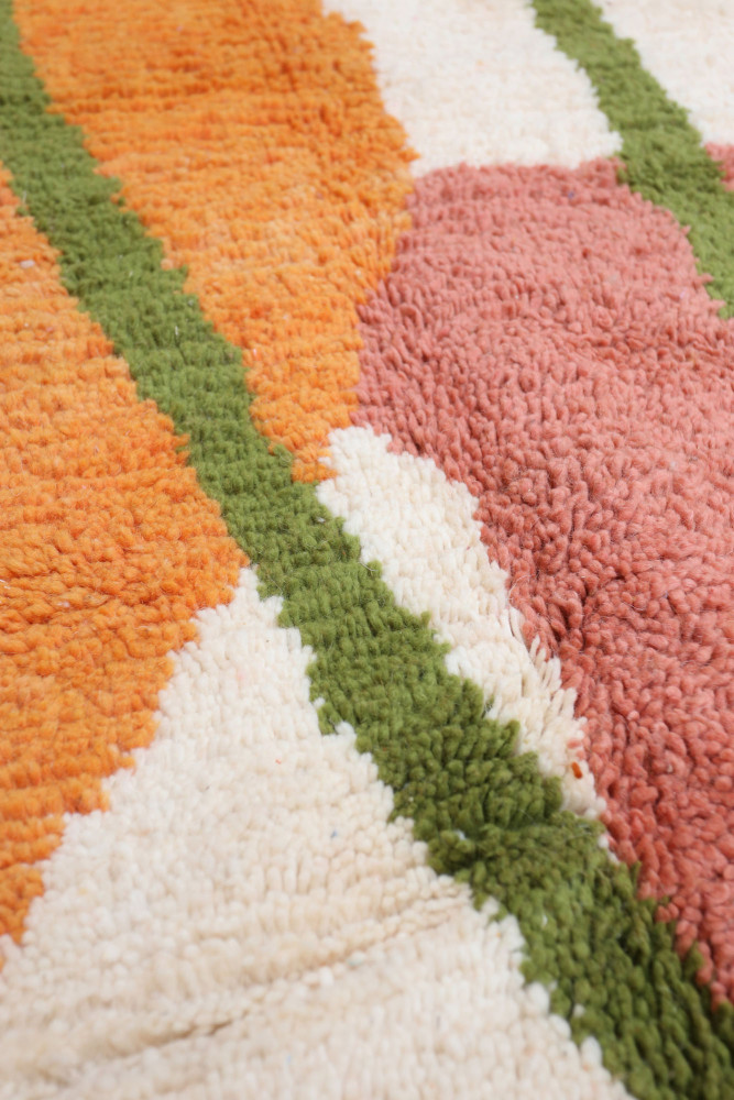 Tapis berbère coloré avec des motifs géométriques en orange, rose, crème et vert, apportant une touche moderne et chaleureuse.