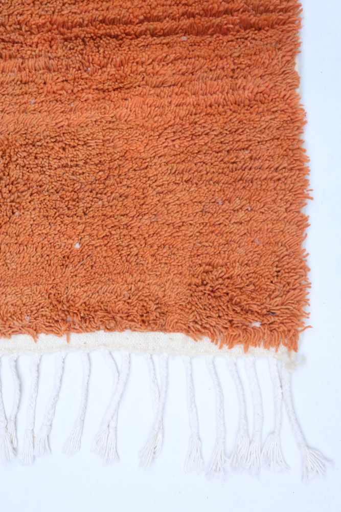 Tapis berbère aux teintes orange chaleureux, avec un motif texturé et des franges blanches élégantes.