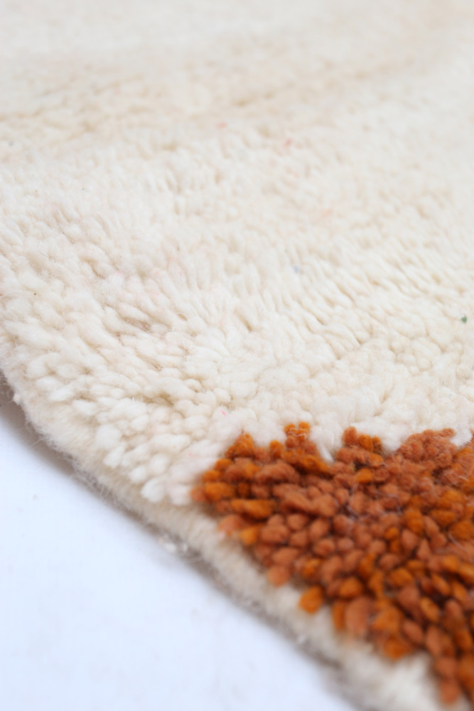 Tapis berbère en laine, couleur crème avec des motifs géométriques orangés, idéal pour ajouter une touche chaleureuse.