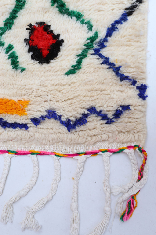 Tapis berbère en laine, style traditionnel avec motifs colorés en rouge, bleu, vert et orange sur un fond crème.