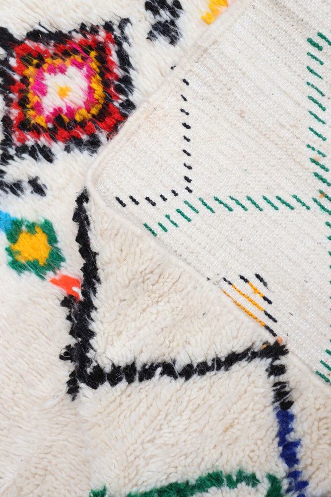 Tapis berbère en laine, avec des motifs géométriques colorés rouges, verts et jaunes sur fond crème.