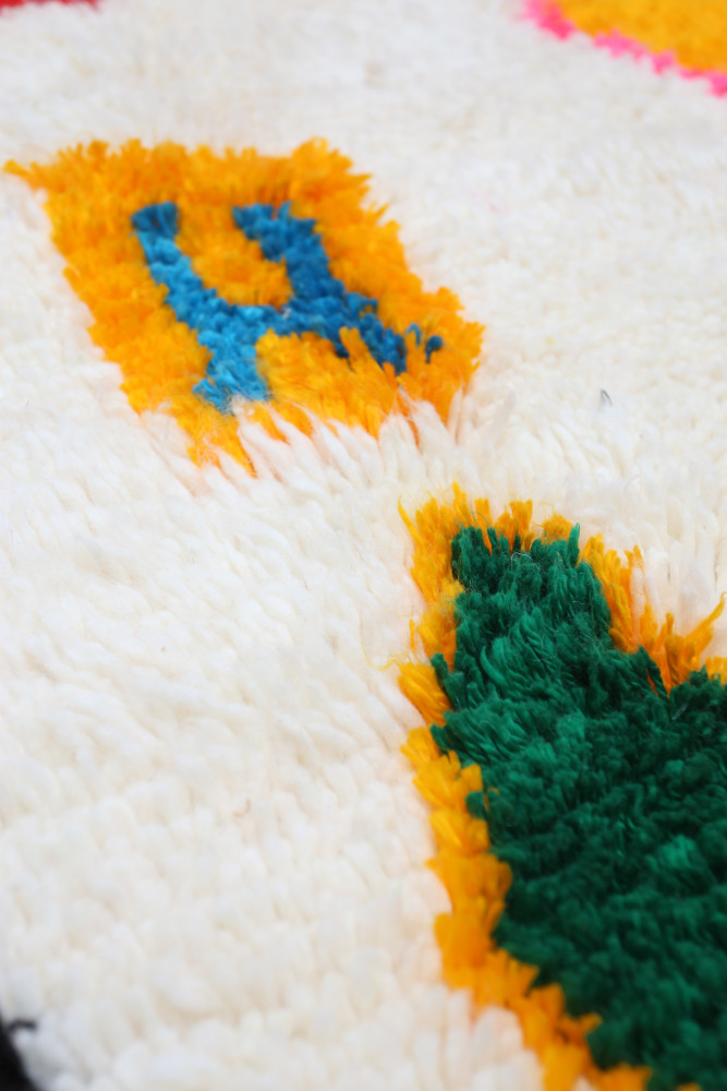 Tapis berbère aux motifs colorés en jaune, bleu et vert sur fond blanc, ajoutant une touche de chaleur à votre intérieur.