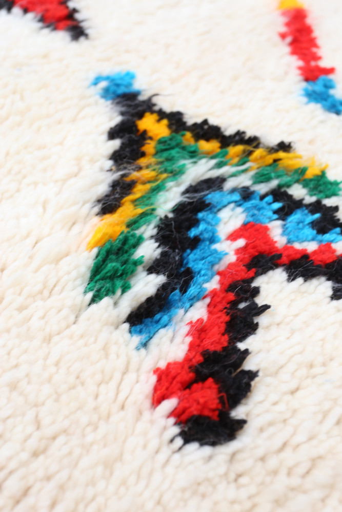 Tapis berbère en laine, avec un fond crème orné de motifs géométriques colorés en vert, bleu, rouge et jaune.
