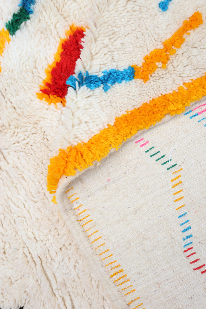 Tapis berbère aux motifs géométriques colorés avec des teintes dominantes de blanc, rouge, bleu et jaune.