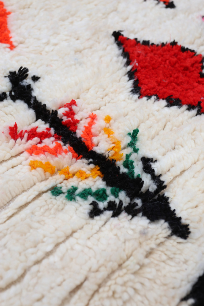 Tapis berbère traditionnel aux motifs floraux colorés sur fond crème avec des touches de rouge et de noir.