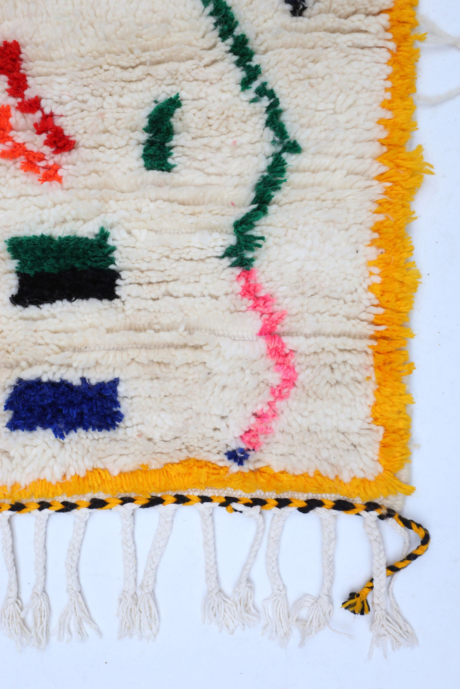 Tapis berbère aux motifs colorés, dominé par des tons beige, orange et bleu, offrant une touche artisanale unique.