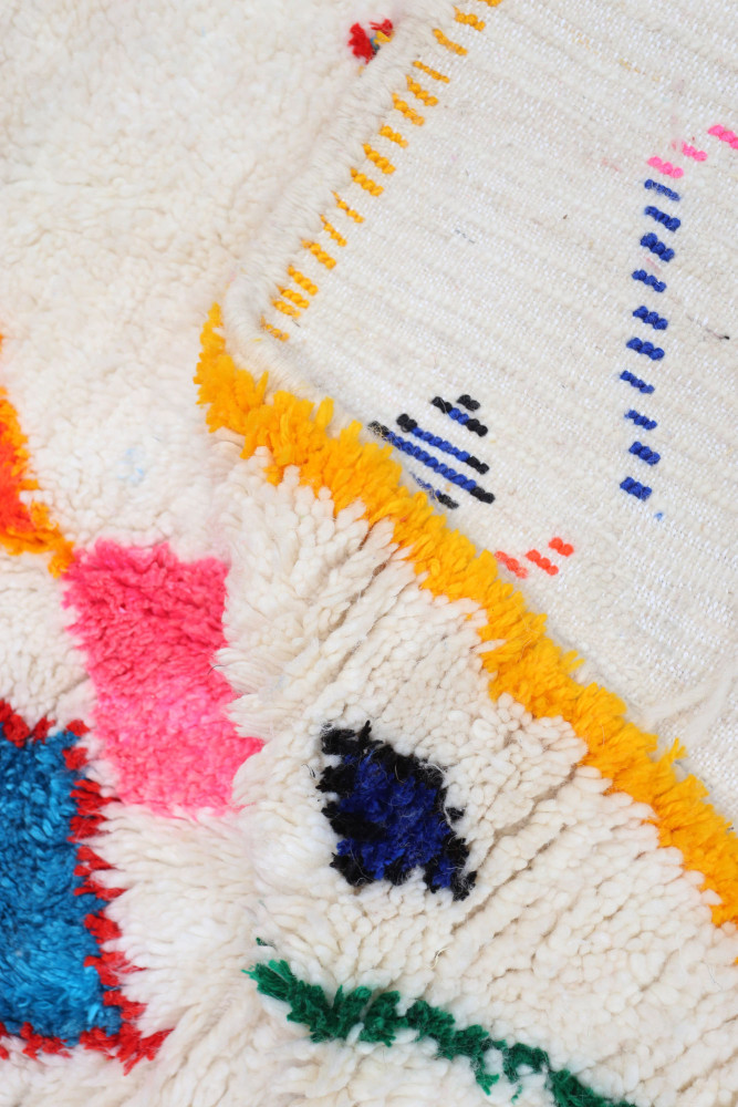 Tapis berbère aux motifs colorés avec des teintes vives de rose, bleu et jaune sur fond crème.