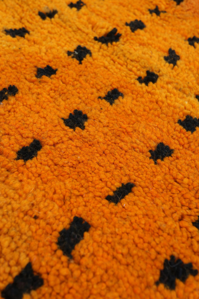 Tapis berbère aux teintes orange vif avec motifs noirs géométriques en pointillé.