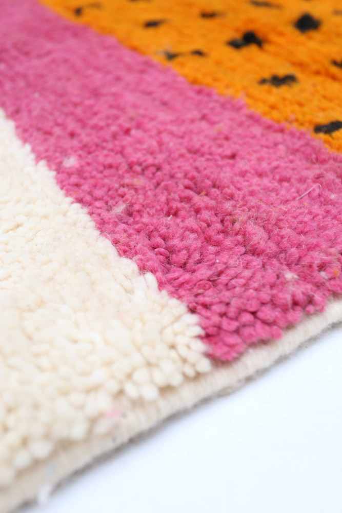 Tapis berbère coloré avec des motifs géométriques, dominé par le rose, l\'orange et le beige.