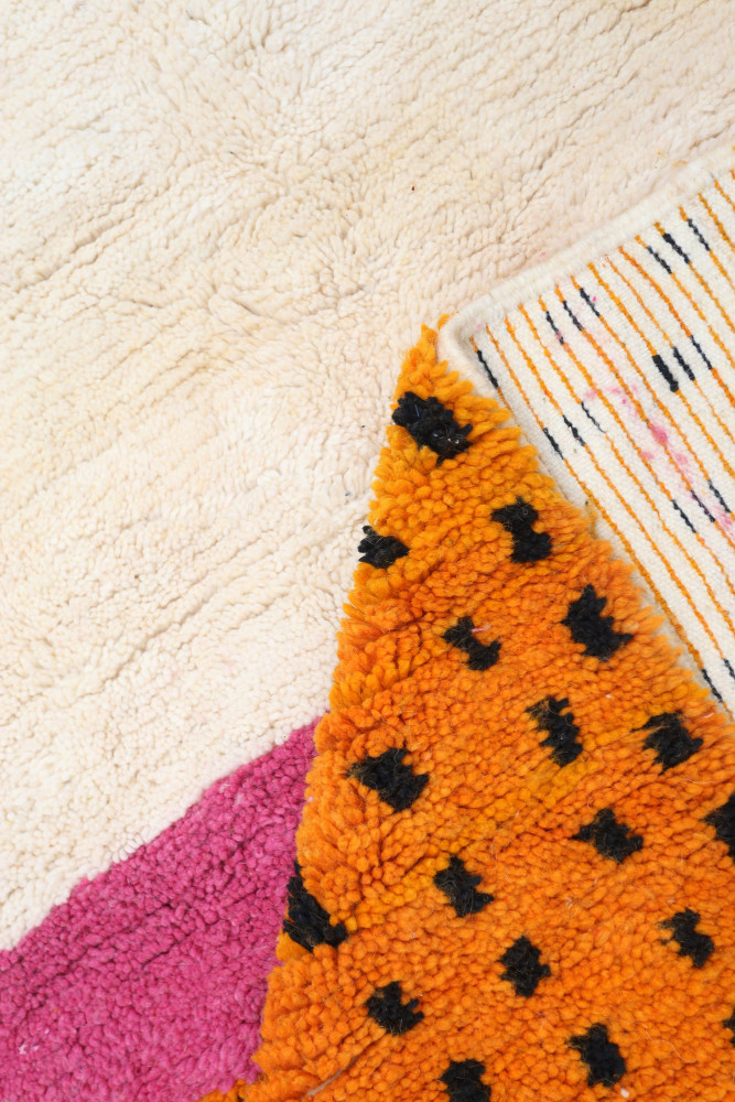 Tapis berbère coloré avec des motifs en orange, rose et noir sur un fond doux, ajoutant du style et de la texture.