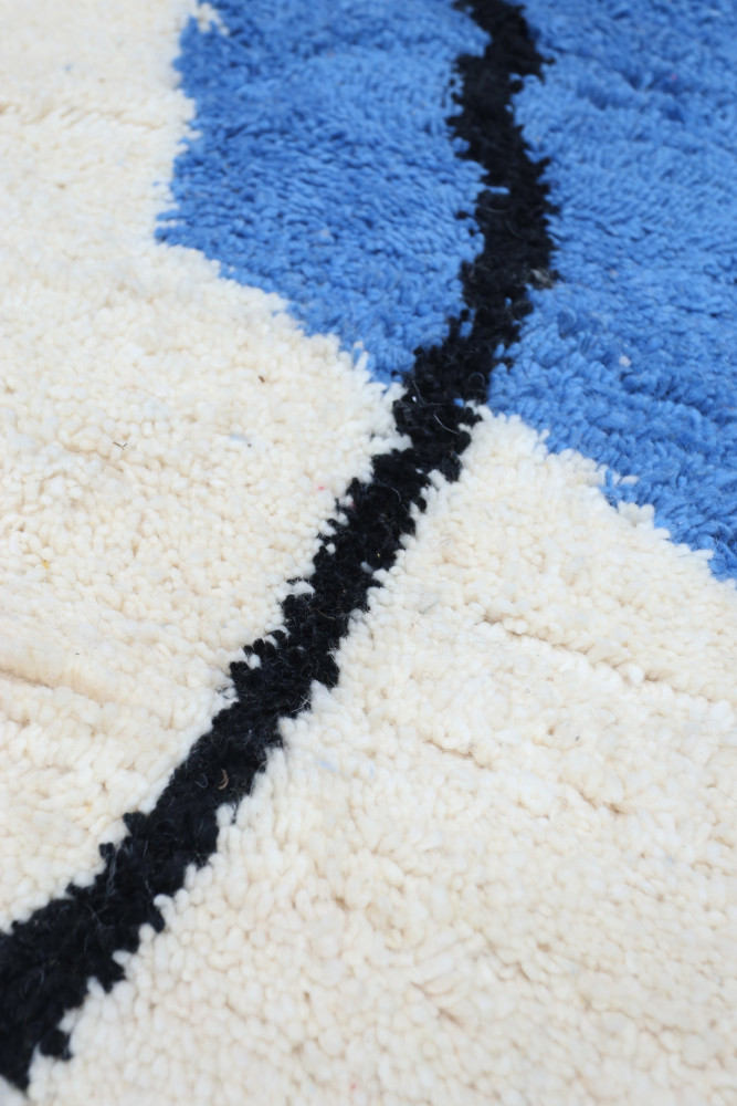 Tapis berbère au style moderne avec des motifs en bleu, noir et beige sur un fond texturé.