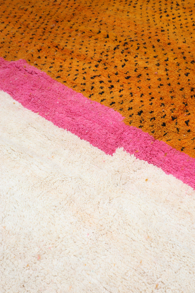 Tapis berbère aux couleurs orange, rose et blanc, avec des motifs graphiques et une texture douce.