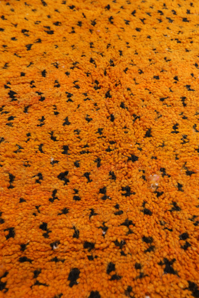 Tapis berbère aux motifs noirs sur fond orange vif, ajoutant chaleur et caractère à votre intérieur.