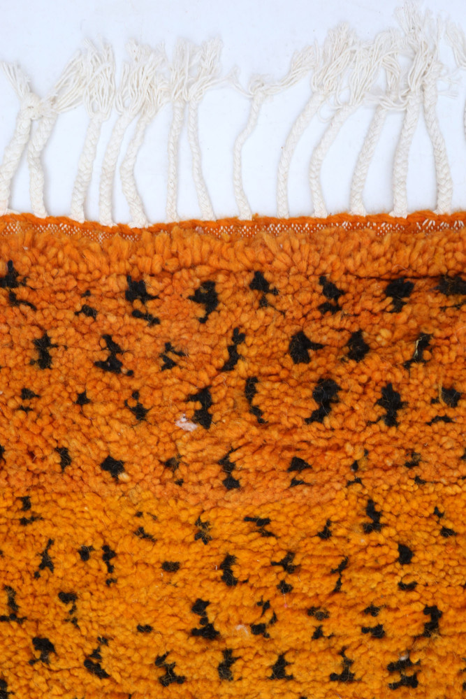 Tapis berbère orange vibrant avec des motifs noirs, texture douce et franges, parfait pour embellir votre intérieur.