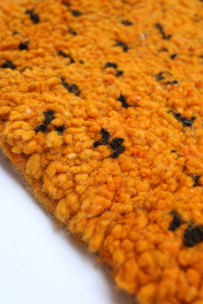 Tapis berbère en laine aux teintes orange vibrant et motifs noirs, ajoutant une touche chaleureuse à votre intérieur.