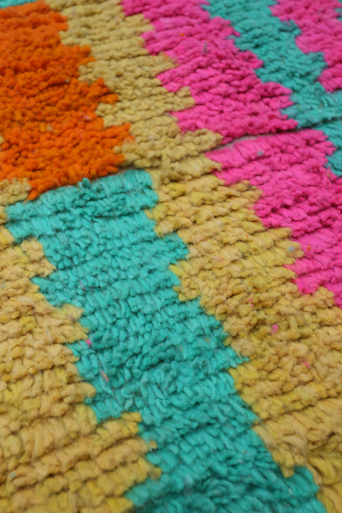 Tapis berbère coloré avec des motifs géométriques en rose, bleu, orange et jaune, apportant une touche contemporaine.