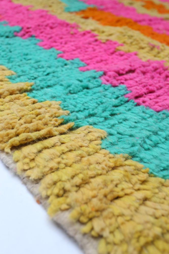 Tapis berbère aux couleurs vives de rose, turquoise et jaune avec des motifs géométriques attrayants.