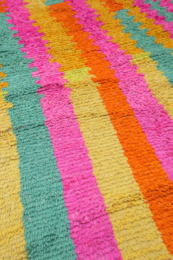 Tapis berbère aux couleurs vives avec des motifs rayés en rose, orange, vert et jaune.