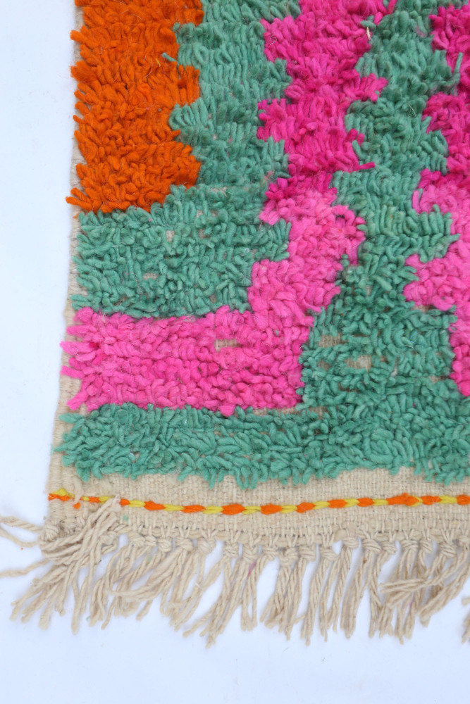 Tapis berbère coloré présentant des motifs géométriques en vert, rose, orange et beige avec des franges élégantes.