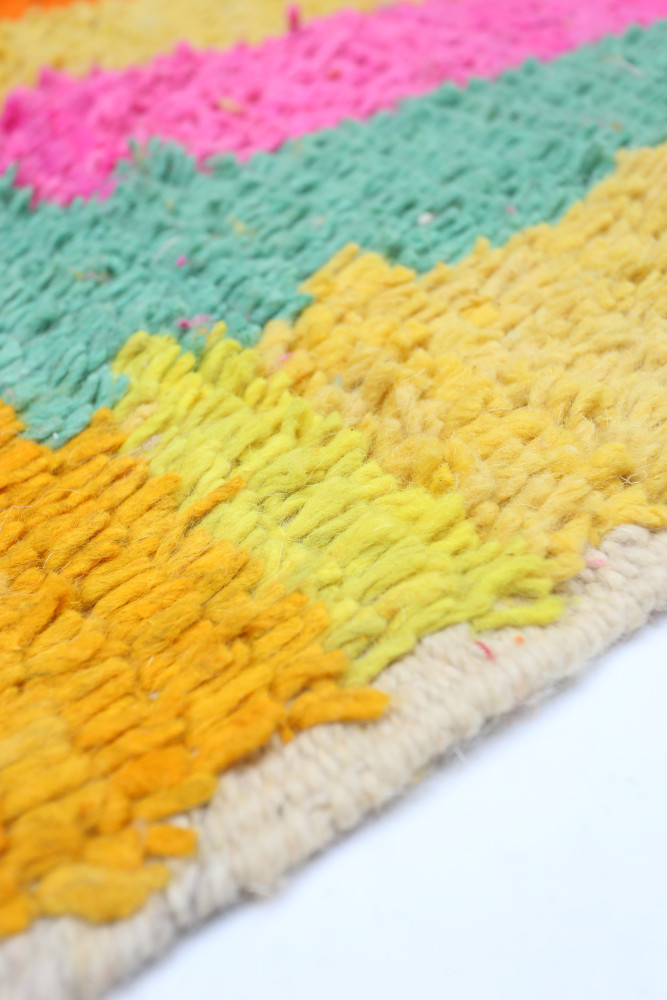 Tapis berbère aux couleurs vives avec des motifs en zigzag dans des teintes de rose, vert, orange et jaune.
