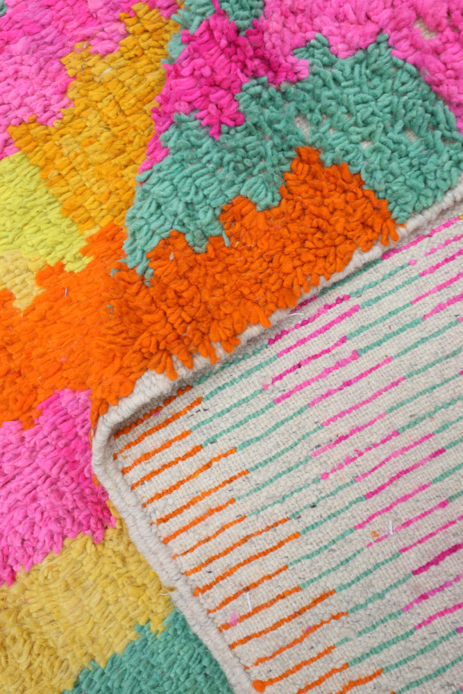 Tapis berbère coloré avec des motifs géométriques vifs en rose, orange, vert et jaune sur un fond clair.
