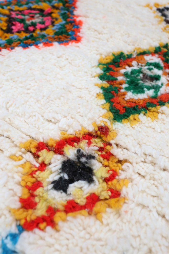 Tapis berbère en laine, aux motifs géométriques colorés avec des teintes de blanc, orange, vert et noir.