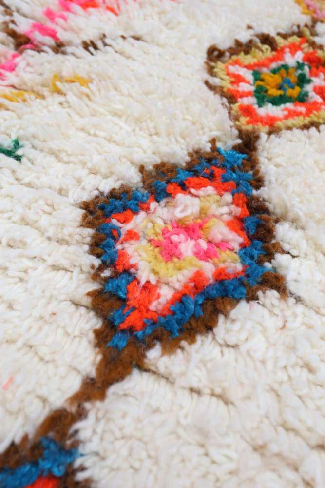 Tapis berbère aux couleurs vives avec des motifs géométriques en rose, bleu et orange sur fond crème.