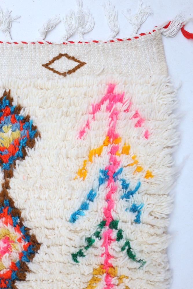 Tapis berbère aux couleurs vives, motifs géométriques et designs floraux sur fond crème.
